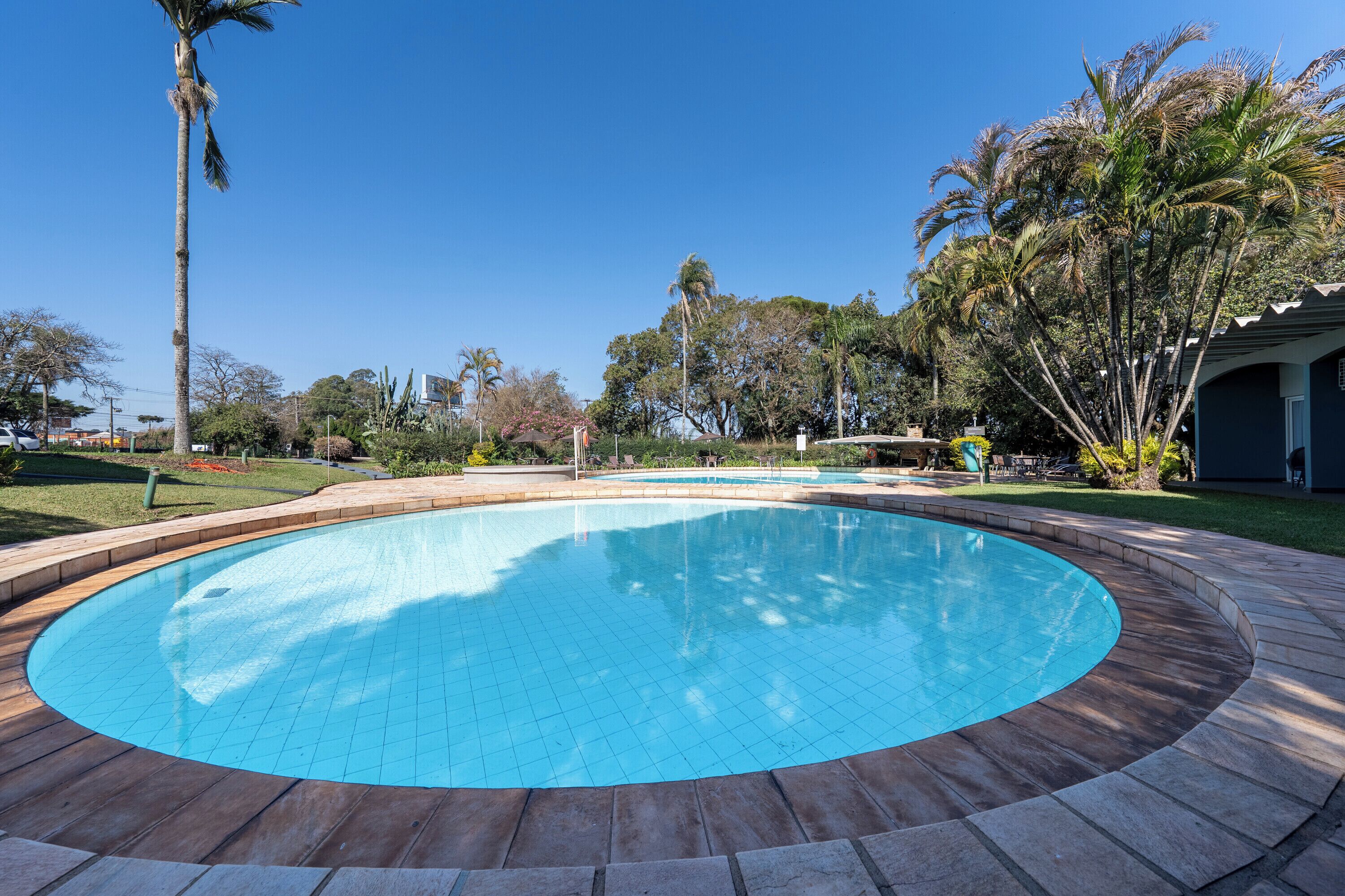 A circular swimming pool with a tiled edge, surrounded by a wooden deck and a stone border.