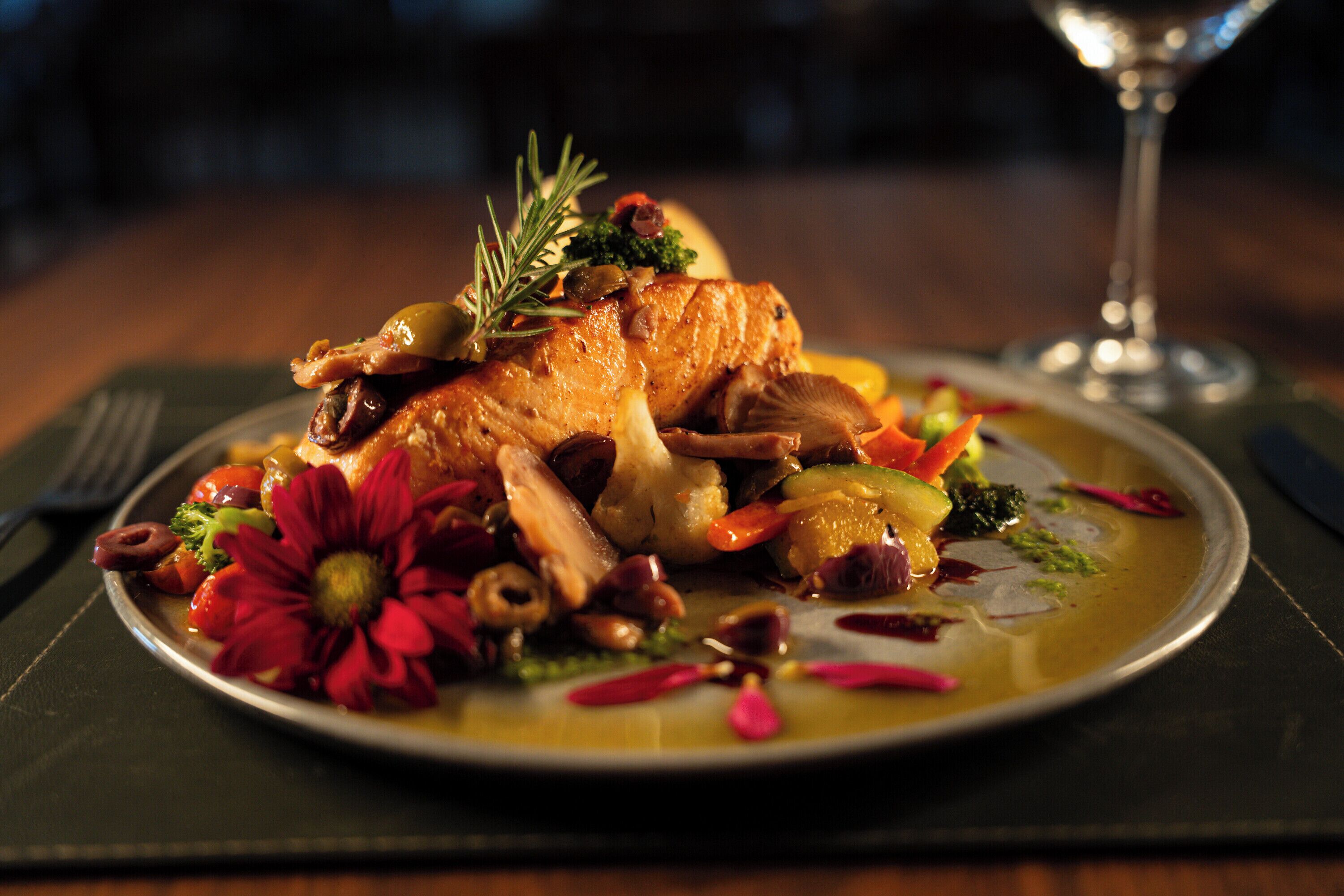 A plate of food with a variety of vegetables and a piece of meat, possibly chicken, garnished with herbs.