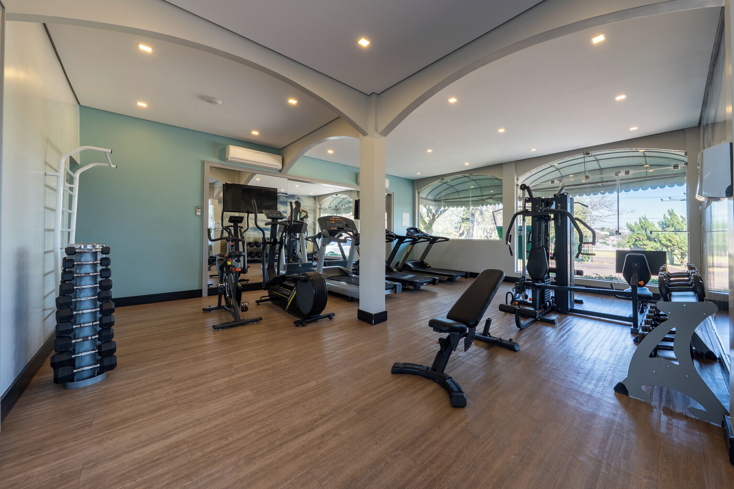 Academia com equipamentos de exercícios, um espelho e vista para o exterior.