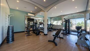 Academia com equipamentos de exercícios, um espelho e vista para o exterior.