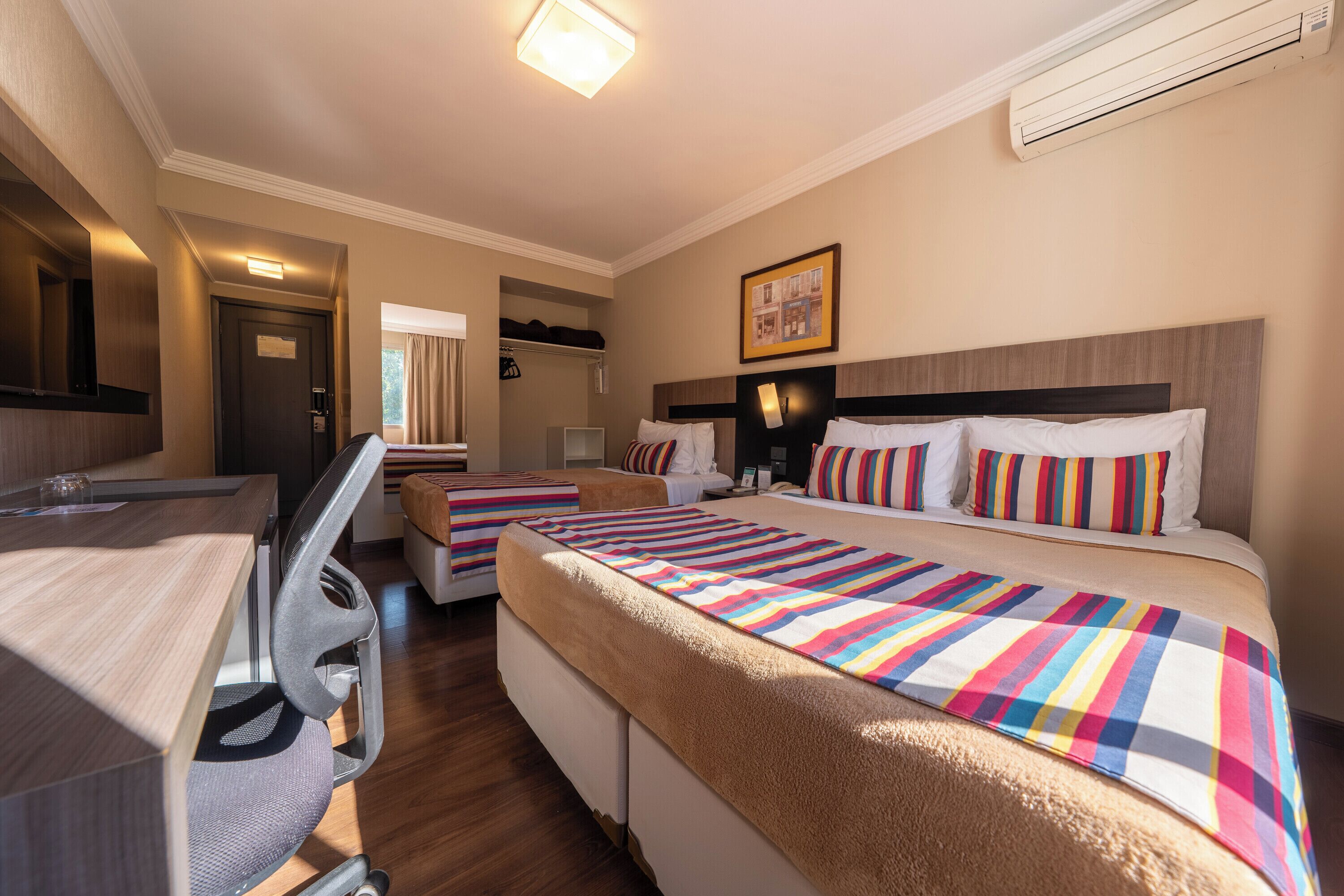 Habitación de hotel con dos camas, un escritorio, una silla, un espejo y una ventana.
