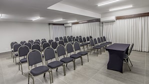 Un salón de conferencias con filas de sillas, una mesa y un equipo de aire acondicionado.