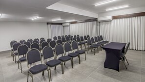 A conference room with rows of chairs, a table, and an air conditioning unit. - Hotel Deville Express Cascavel (Cascavel)