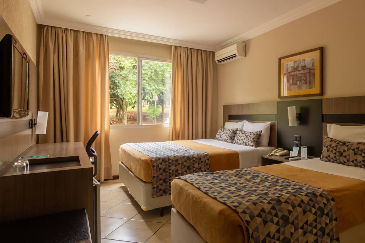 A hotel room with two beds, a desk, and a window with curtains.