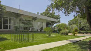 Un edificio de estilo arquitectónico moderno, un camino pavimentado y una zona verde bien cuidada con árboles y un pequeño parque infantil.