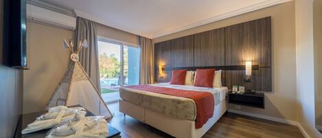 Quarto de hotel com cama, mesa de cabeceira, televisão, janela com cortinas e uma estrutura semelhante a uma tenda.