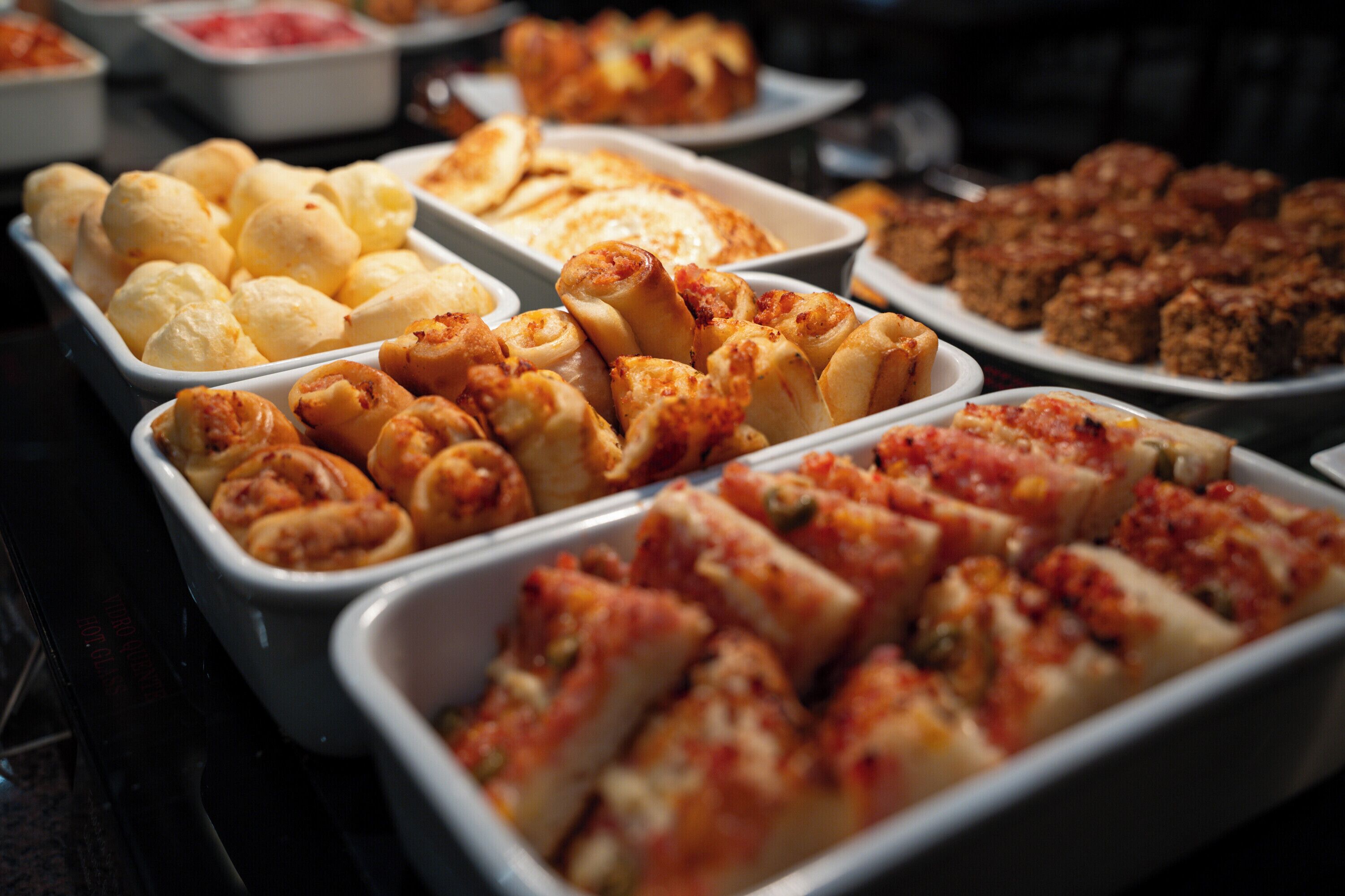 Un bufé con diferentes opciones de comida, como panecillos, pasteles y porciones de pizza.