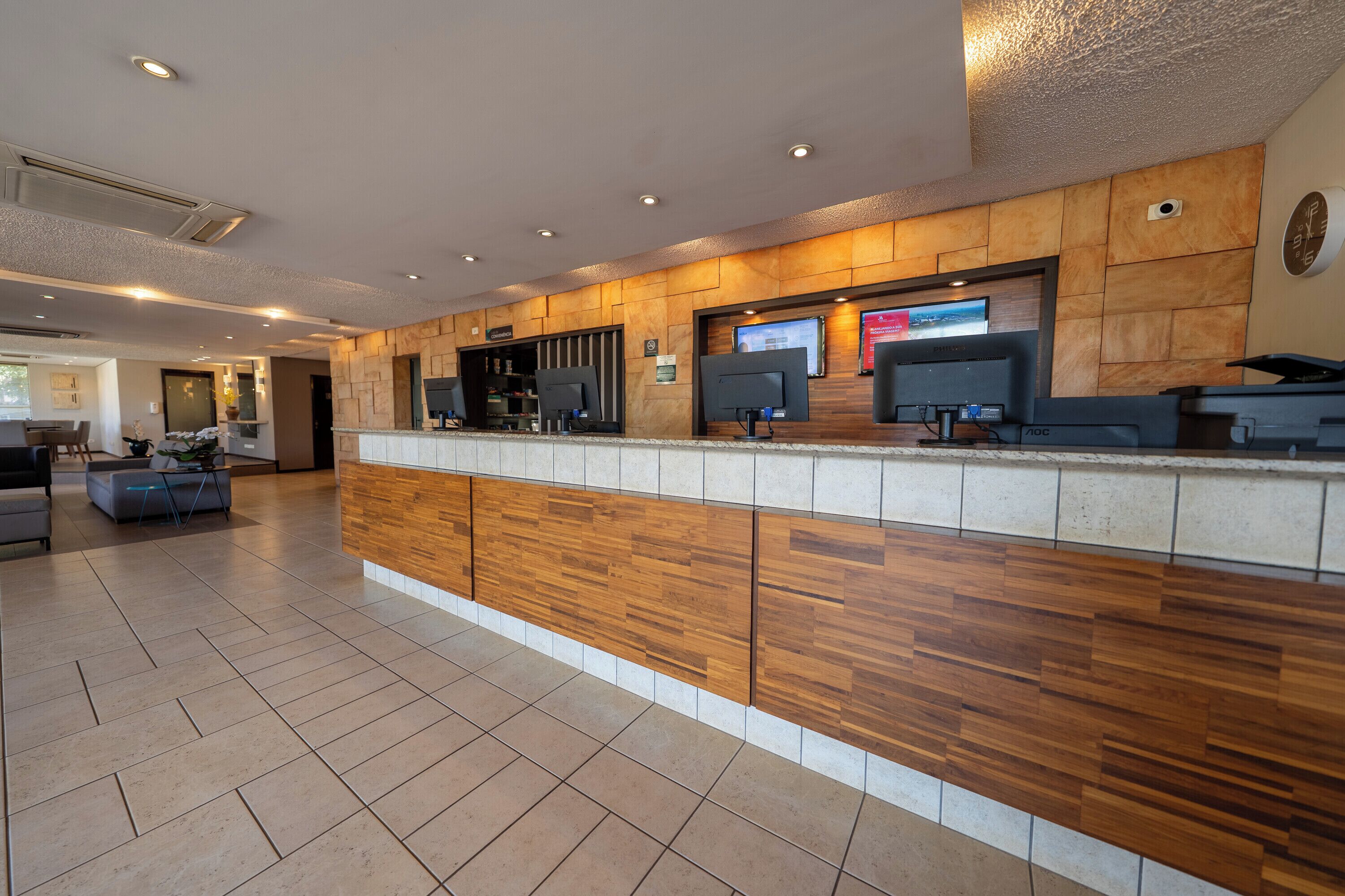 Un espace d’accueil avec un comptoir en bois, plusieurs écrans d’ordinateur et une horloge au mur.