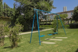 A playground with swings and a paved path. - Hotel Deville Express Cascavel (Cascavel)