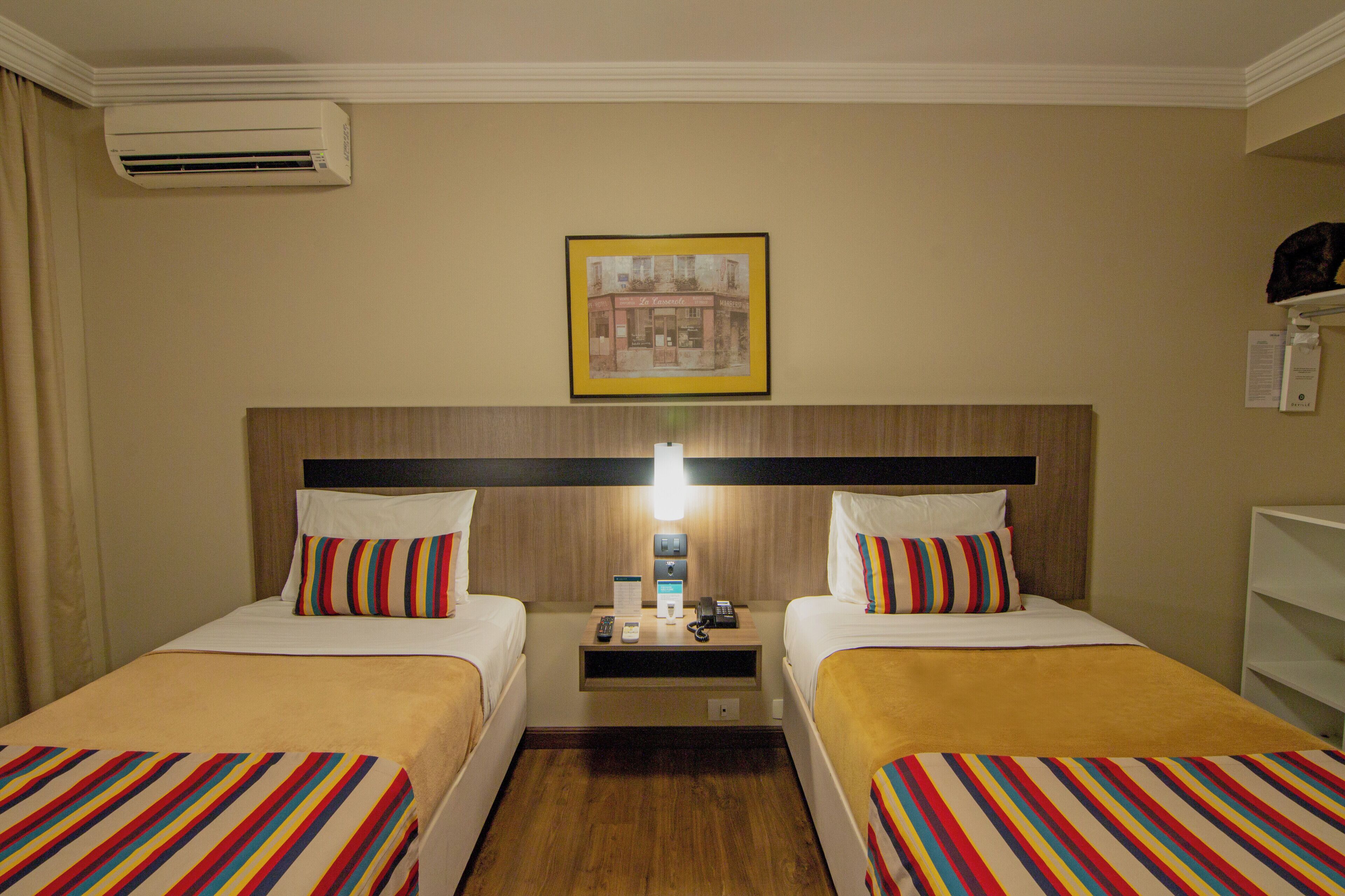 Habitación de hotel con dos camas, una mesita de noche, una lámpara y un cuadro en la pared.