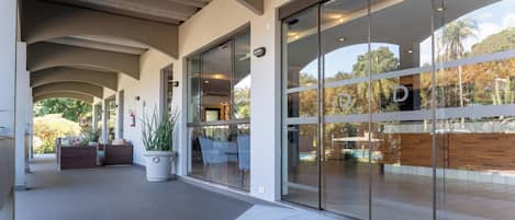 Entrada de un edificio moderno con un vestíbulo techado, puertas de cristal y asientos al aire libre.