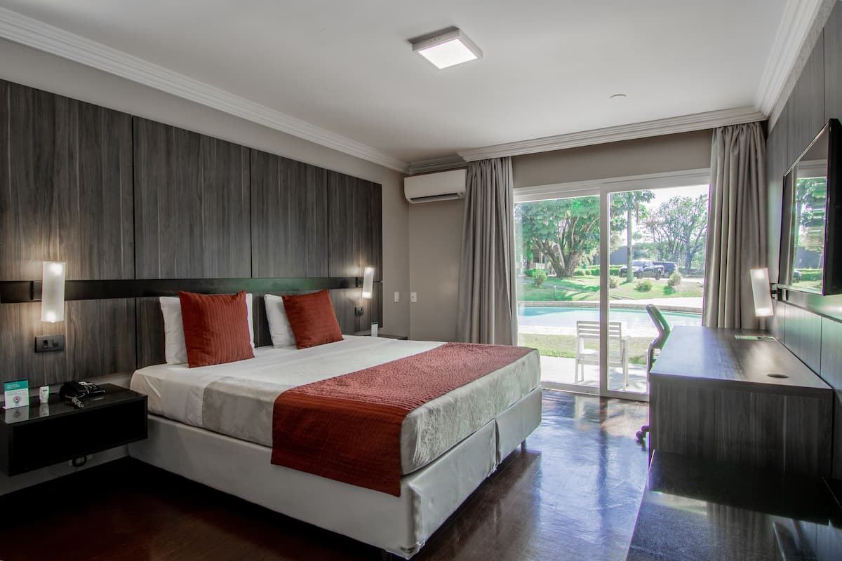 A modern hotel room with a large bed, a desk, and a view of a swimming pool.