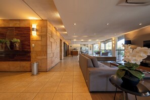 A modern hotel lobby with a reception desk, a seating area, and large windows. - Hotel Deville Express Cascavel (Cascavel)