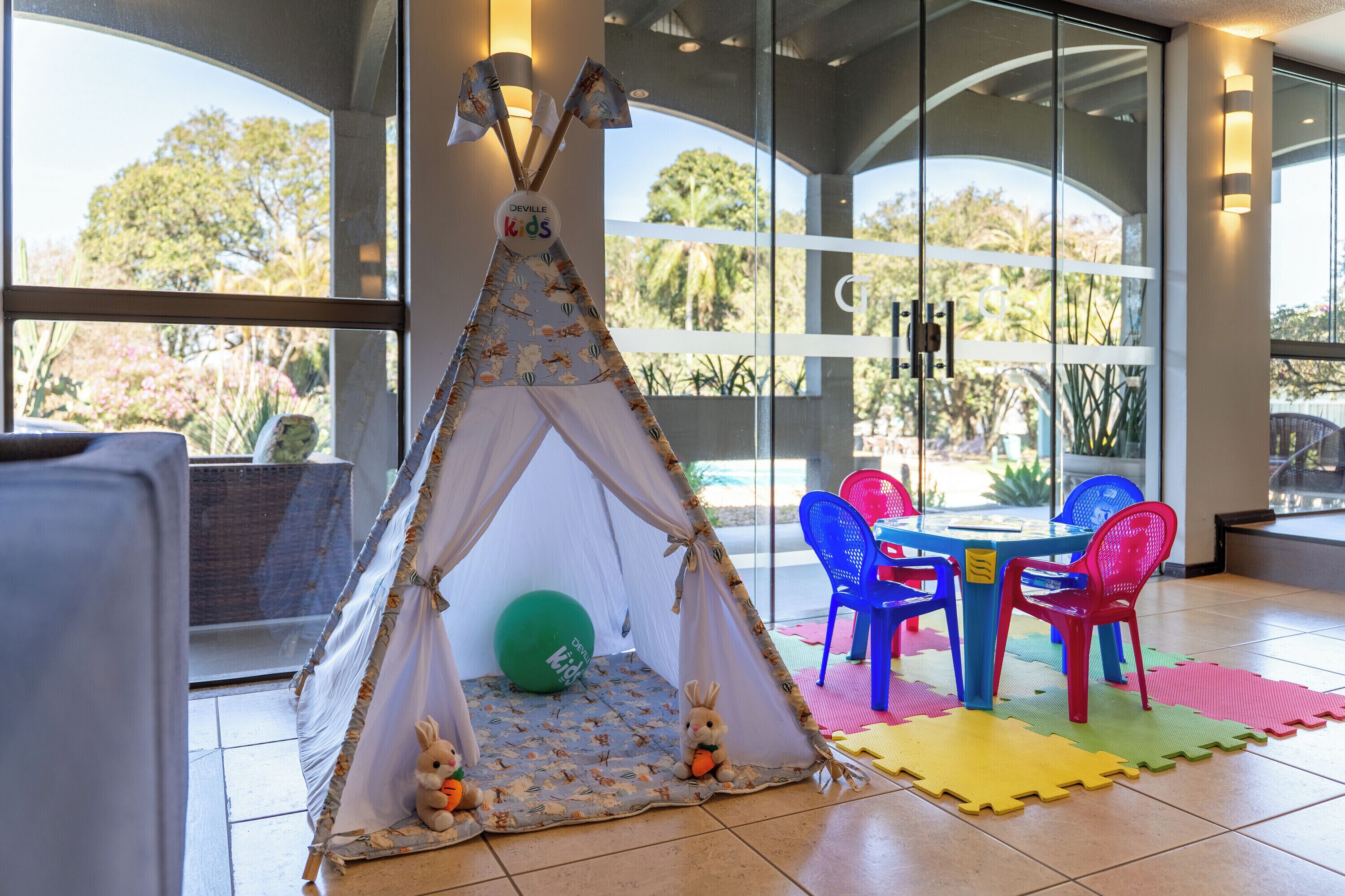 Zona de juegos con un tipi, sillas coloridas y una mesa con un tapete.