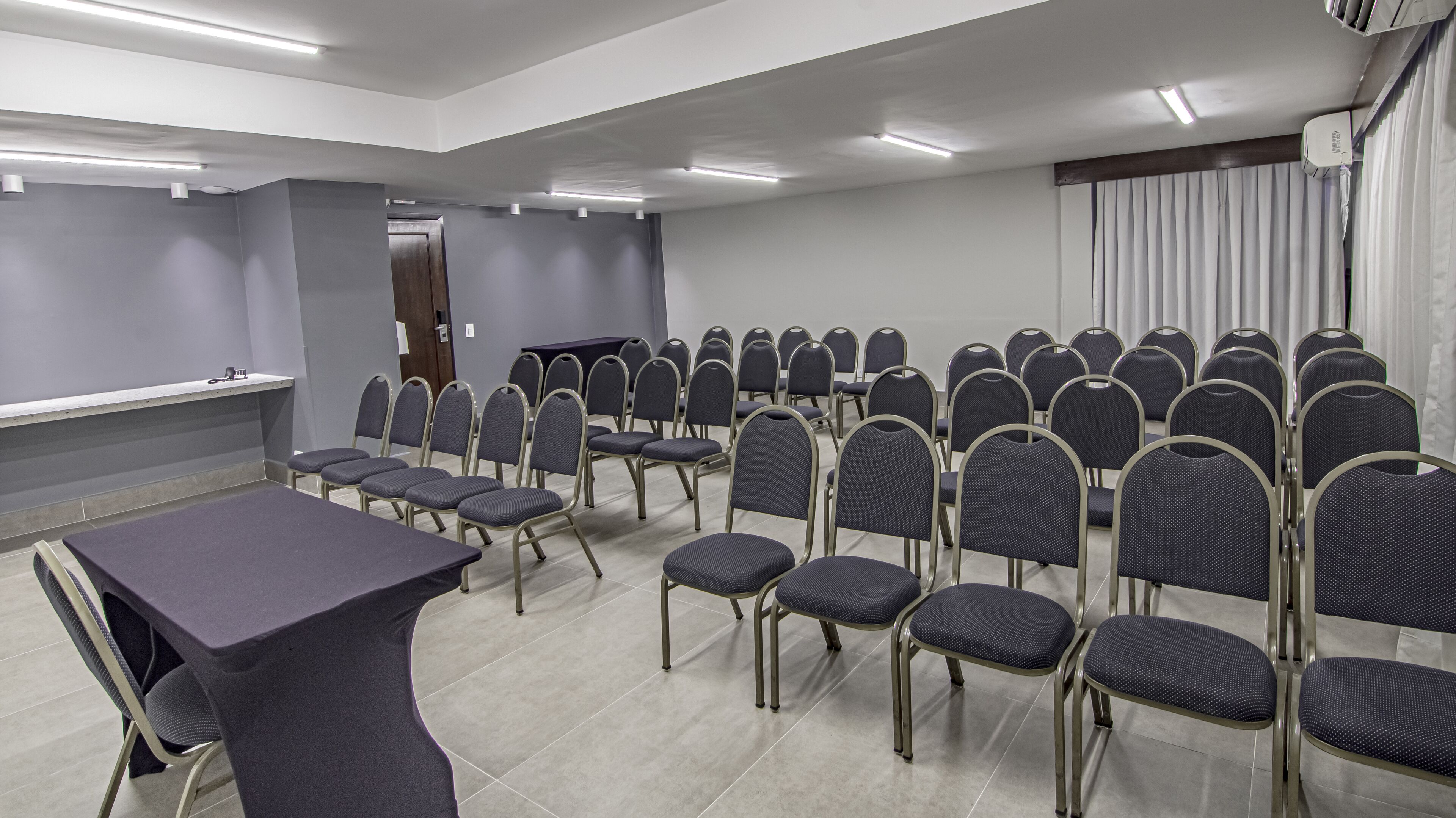 Un salón de conferencias con filas de sillas, una mesa larga y un atril.