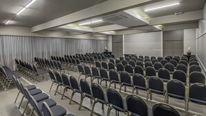 Un salón de conferencias con filas de sillas, un atril y cortinas.