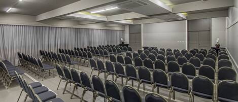 A conference room with rows of chairs, a podium, and curtains.