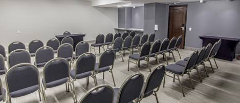 A conference room with rows of chairs and a table, grey walls, and a door.