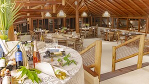 Un amplio comedor con varias mesas redondas, vigas de madera y lámparas de mimbre colgantes.
