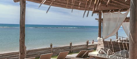A wooden deck with lounge chairs and a canopy overlooking the ocean.
