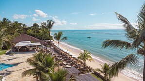 Un hotel frente a la playa con piscina, asientos a la orilla del mar y palmeras.