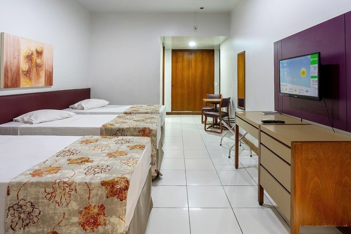 Hotelkamer met twee bedden, een bureau, een stoel, een televisie en een houten deur.