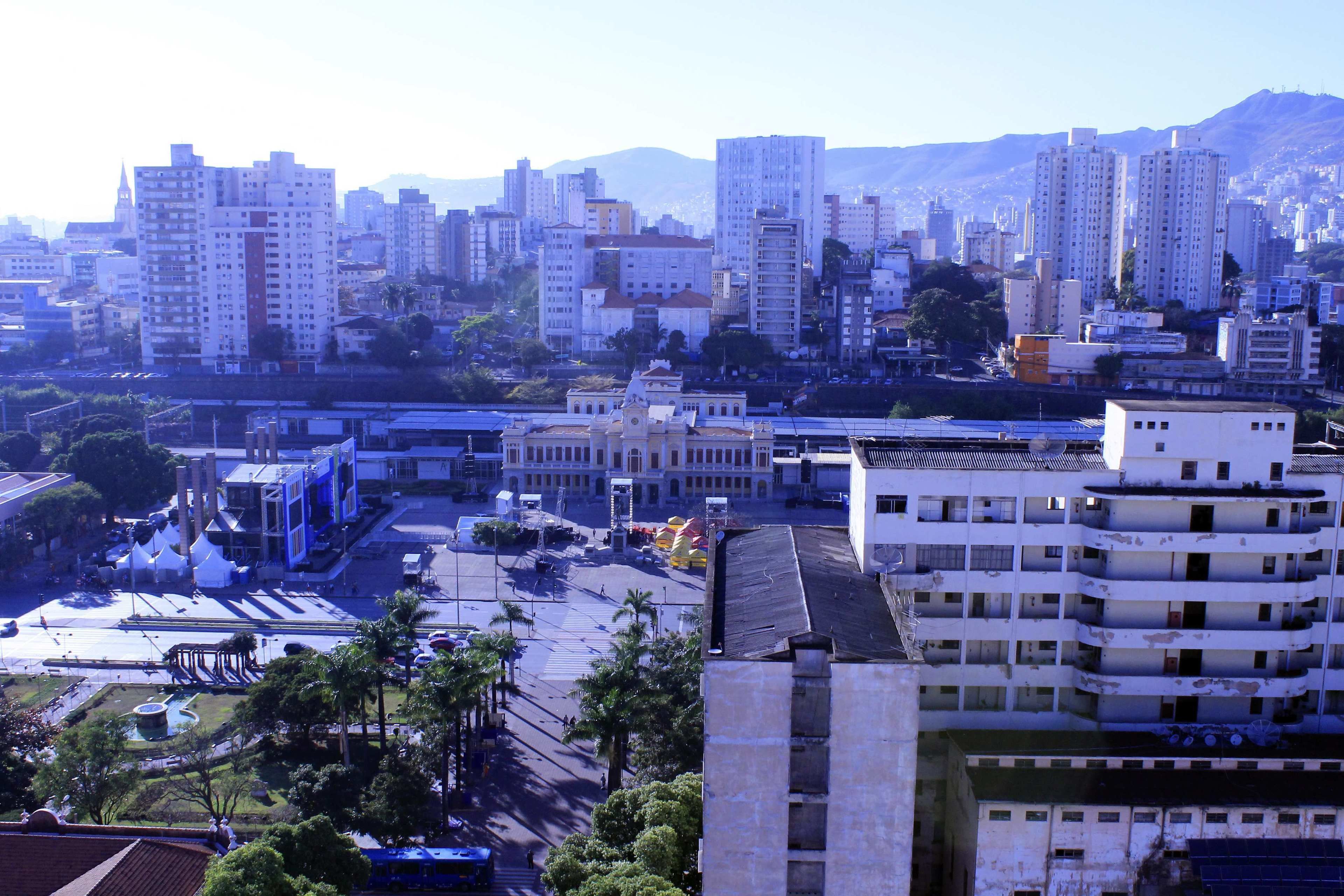 A cityscape with high-rise buildings, a central plaza with palm trees, and a large building with a clock tower.