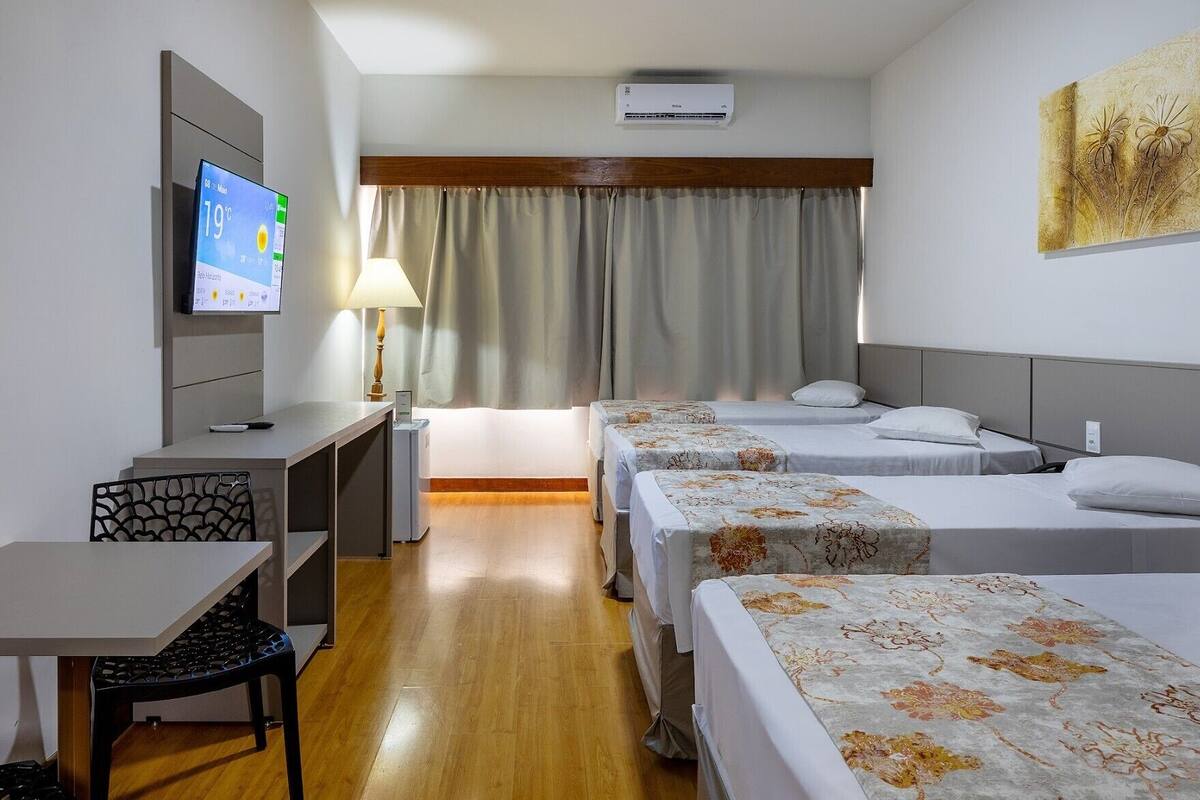 Hotellihuone, jossa on työpöytä, kaksi sänkyä, televisio ja lamppu.
