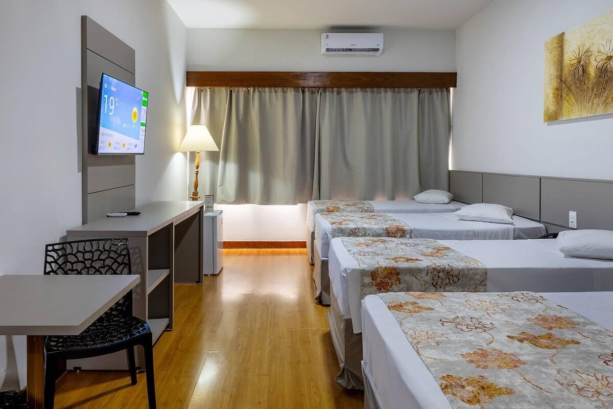 A hotel room with two beds, a desk, a chair, a TV, and a window with curtains.