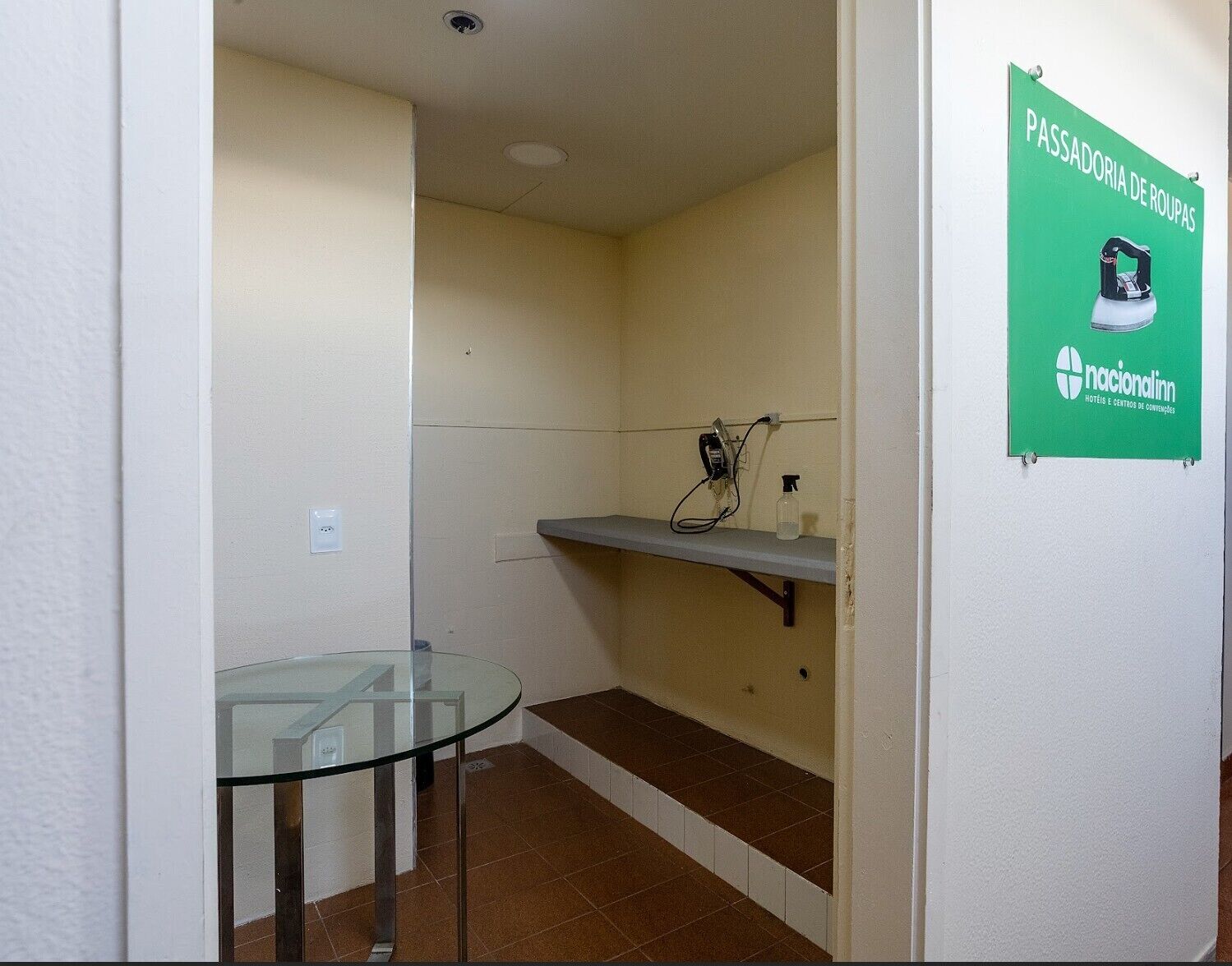 A small room with a glass table, a shelf with a bottle, and a wall-mounted sign.