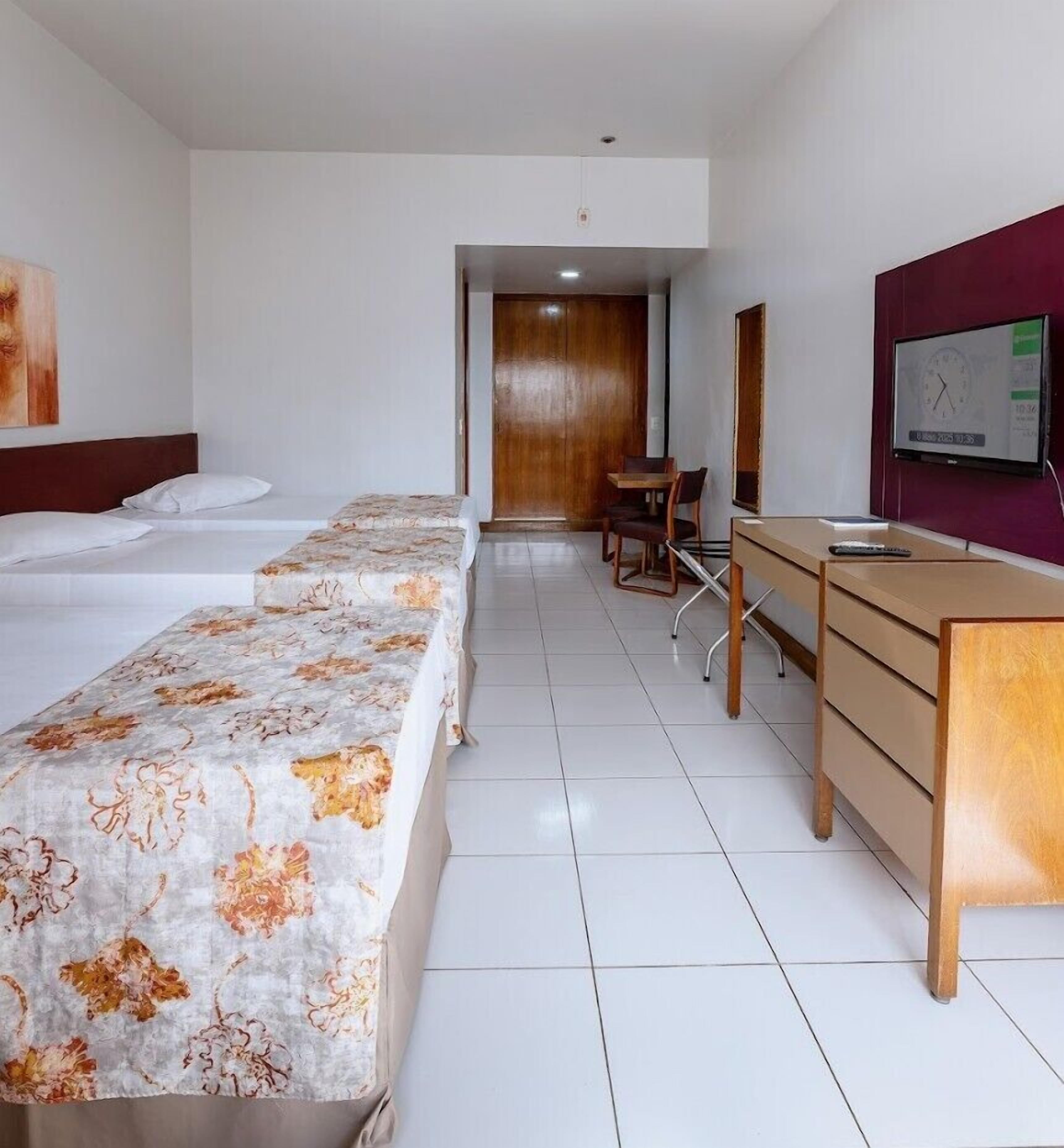 Habitación de hotel con dos camas, un escritorio, una silla, un televisor y una puerta que da a un baño.