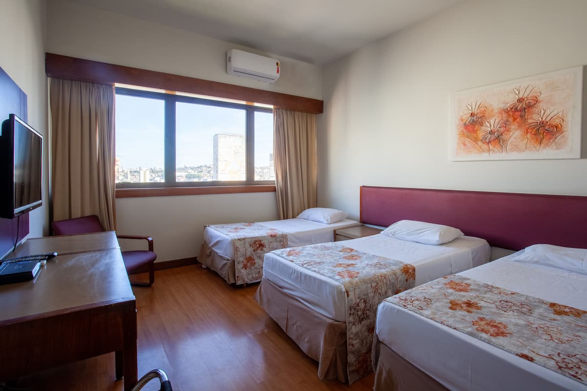 Hotellihuone, jossa on kaksi erillistä sänkyä, työpöytä tuolilla, televisio ja ikkuna, jossa on verhot.