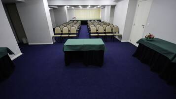 Un salón de conferencias con filas de sillas, una mesa con mantel verde y una puerta a la derecha.