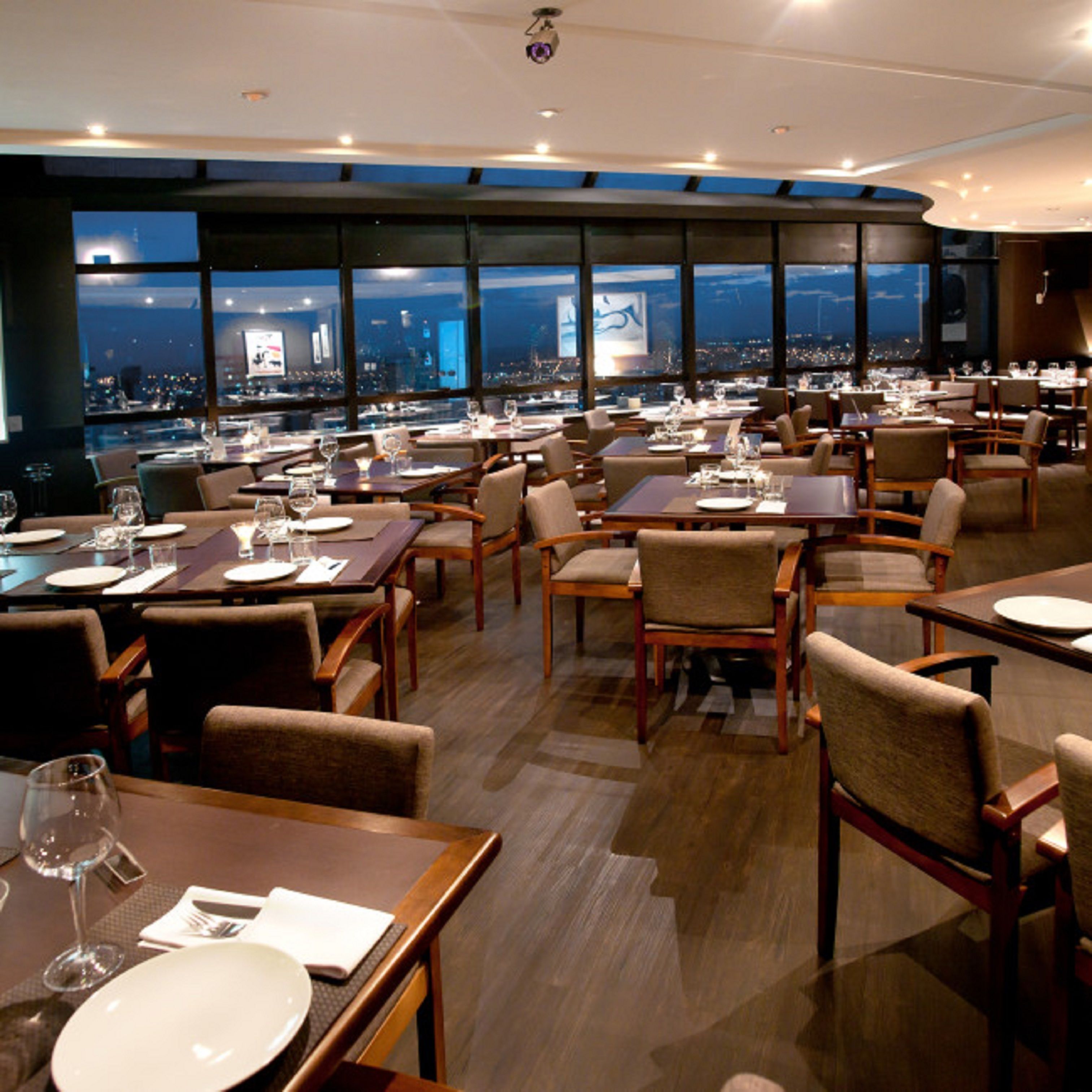 A restaurant with multiple tables and chairs, large windows with a city view, and a modern interior design.