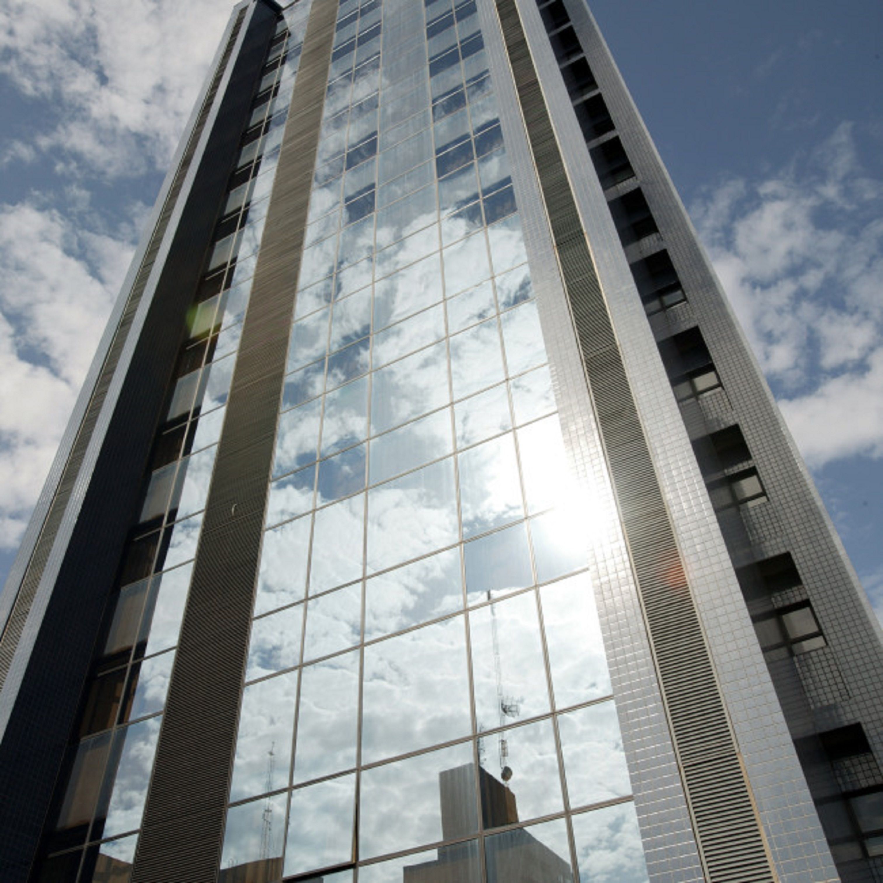 Un edificio alto y moderno con ventanas de vidrio reflectante y un cielo despejado al fondo.