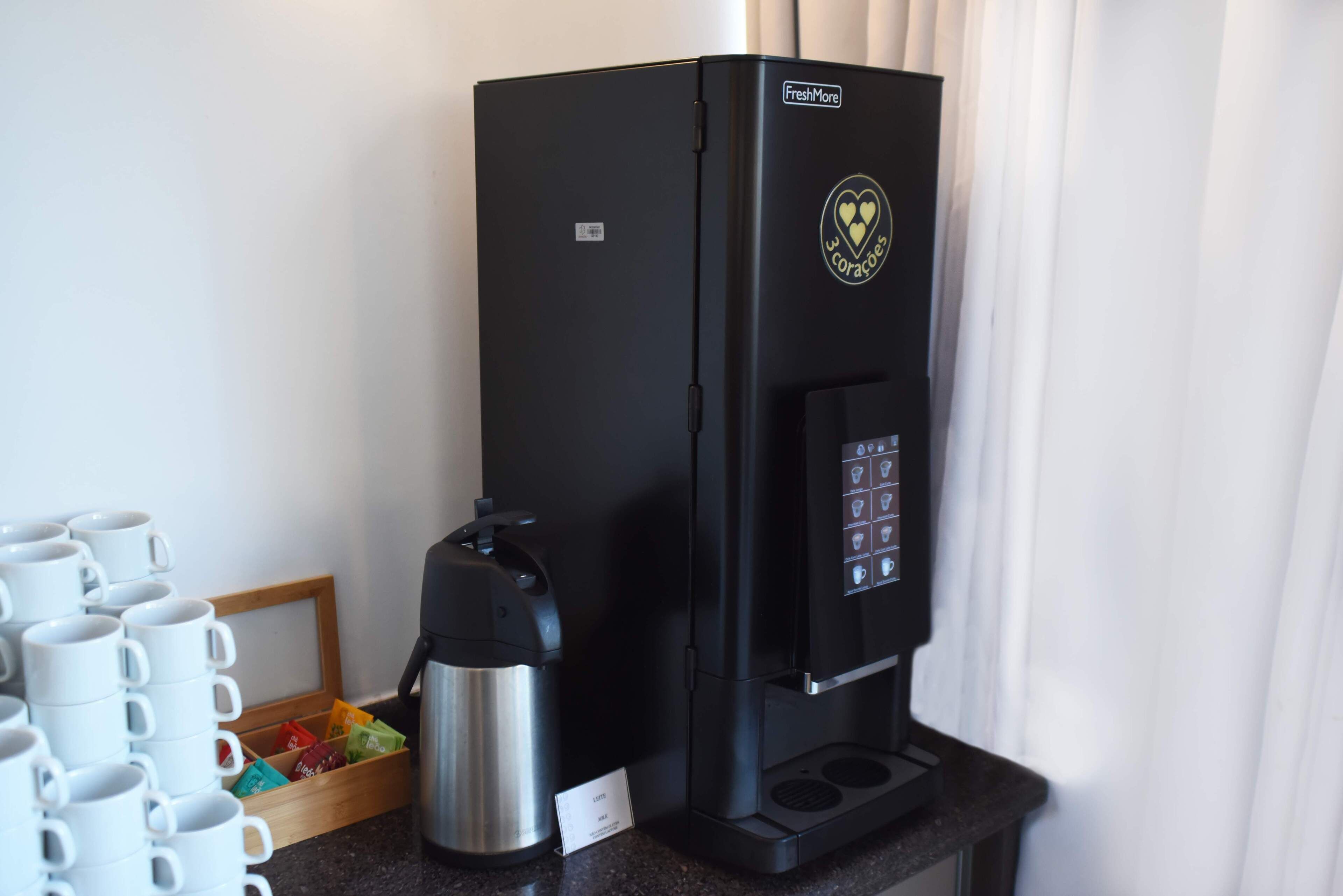 Une machine à café noire ornée d’un logo en forme de cœur, une cafetière en acier inoxydable et un plateau rempli de capsules de café de différentes couleurs.
