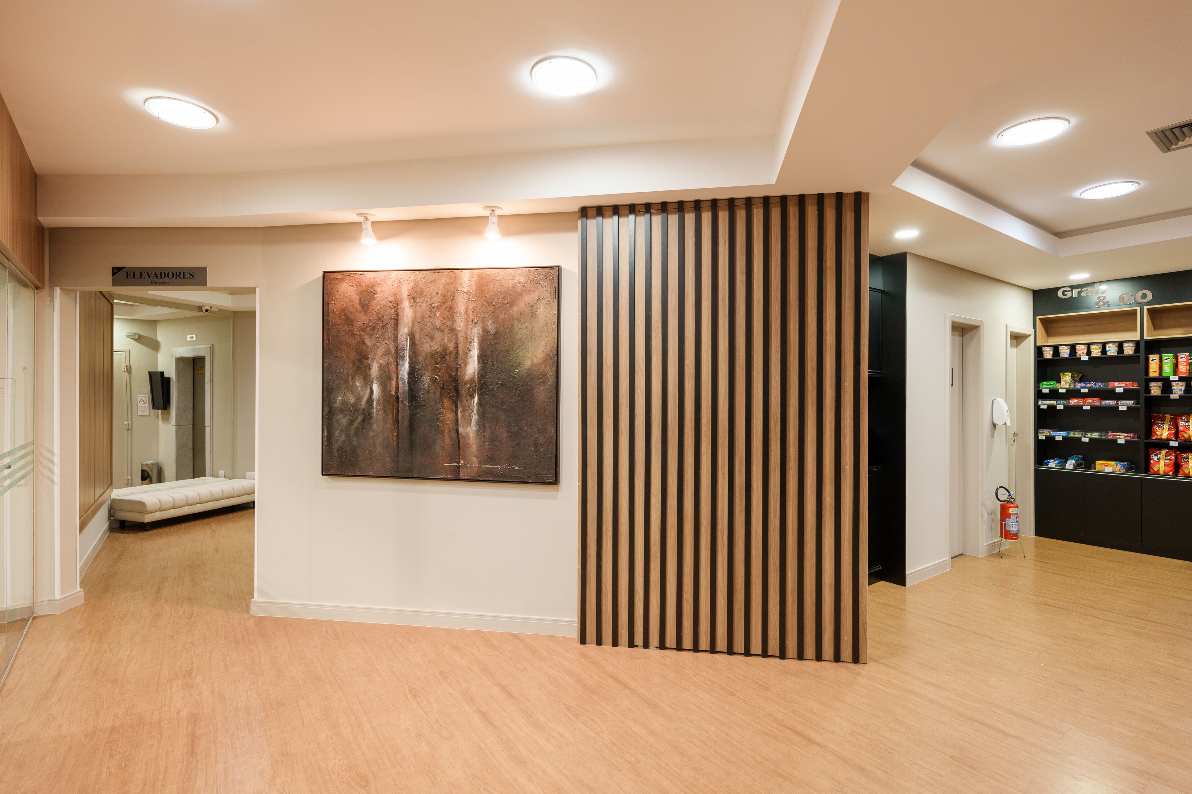 A modern interior with a wooden floor, a large abstract painting, a vending machine, and a sign for 'Elevadores'.