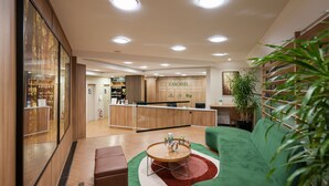 A modern reception area with a wooden reception desk, a green sofa, and a round coffee table. - Central Park Hotel by Bourbon (Cascavel)