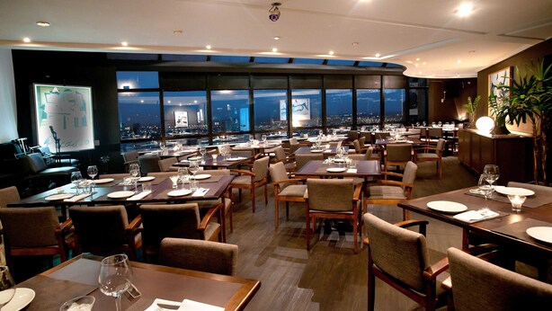 A restaurant with multiple tables and chairs, large windows with a city view, and a modern interior design. - Central Park Hotel by Bourbon (Cascavel)
