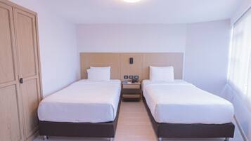 Camera d'albergo con due letti singoli, un armadio in legno, un comodino con una lampada e una finestra con tende.