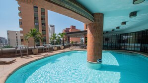 A swimming pool with a tiled edge, a palm tree, and a covered seating area. - Hotel Dann Cali (Cali)