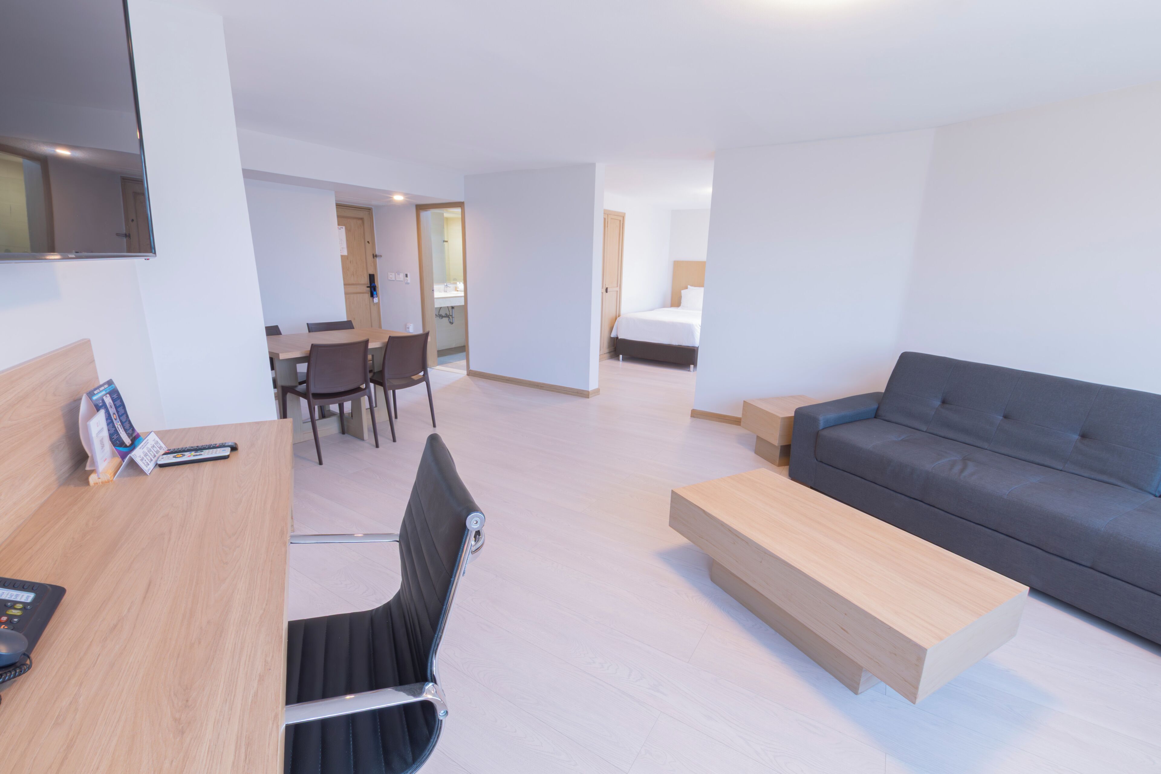 Una habitación de hotel moderna con sofá, escritorio con computadora, silla, cama y zona de comedor.
