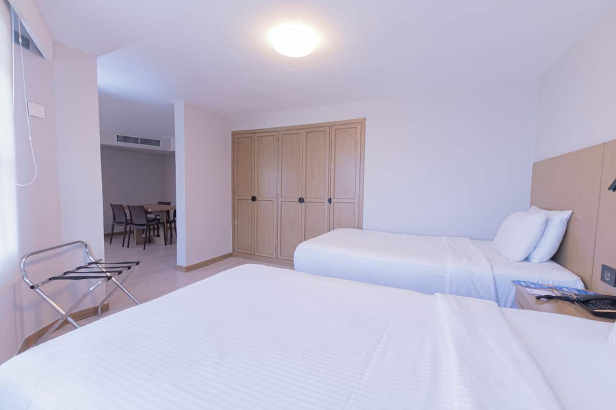 A hotel room with two beds, a desk, and a wardrobe.