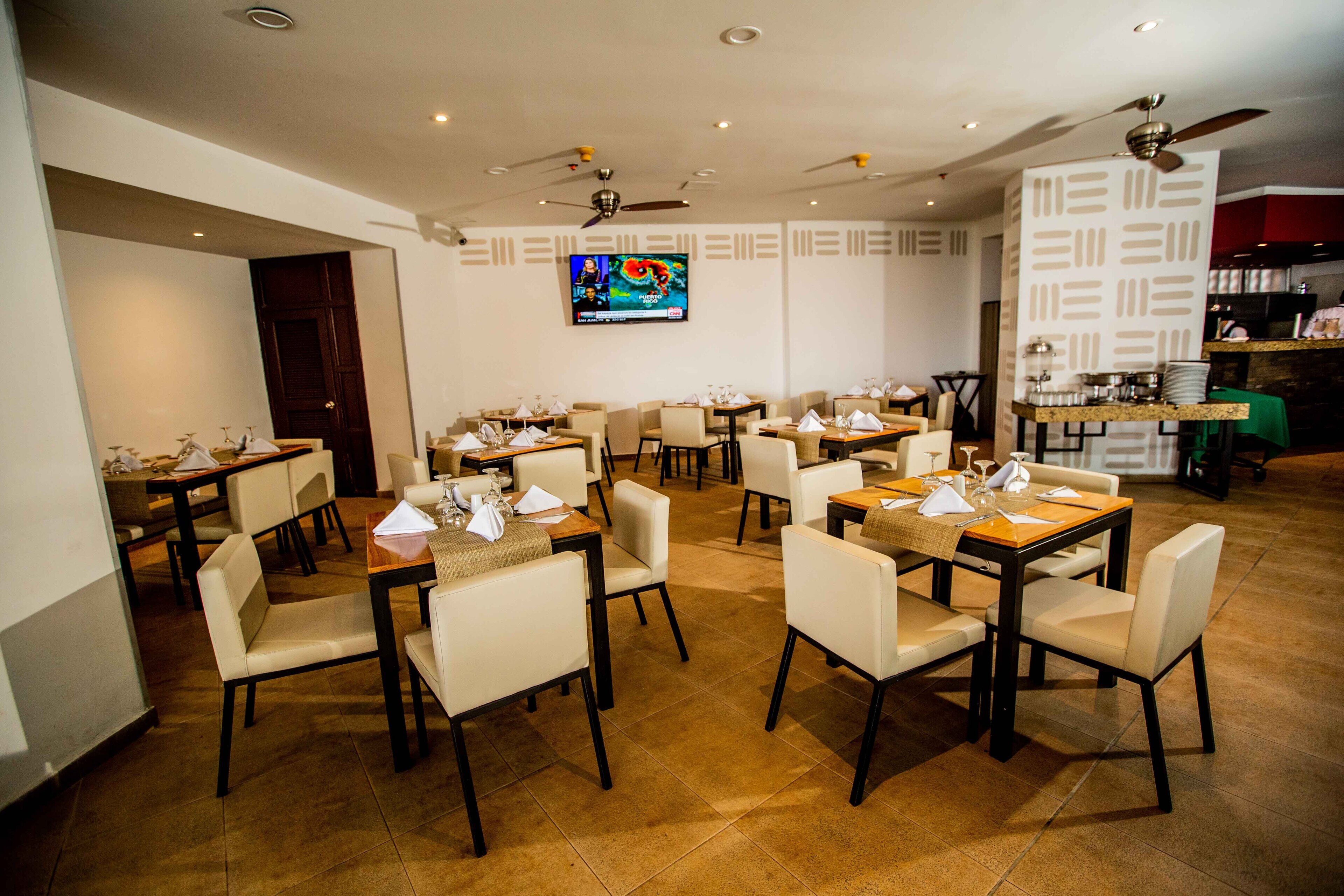 Un restaurant doté de nombreuses tables et chaises, de ventilateurs de plafond et d’un téléviseur fixé au mur.
