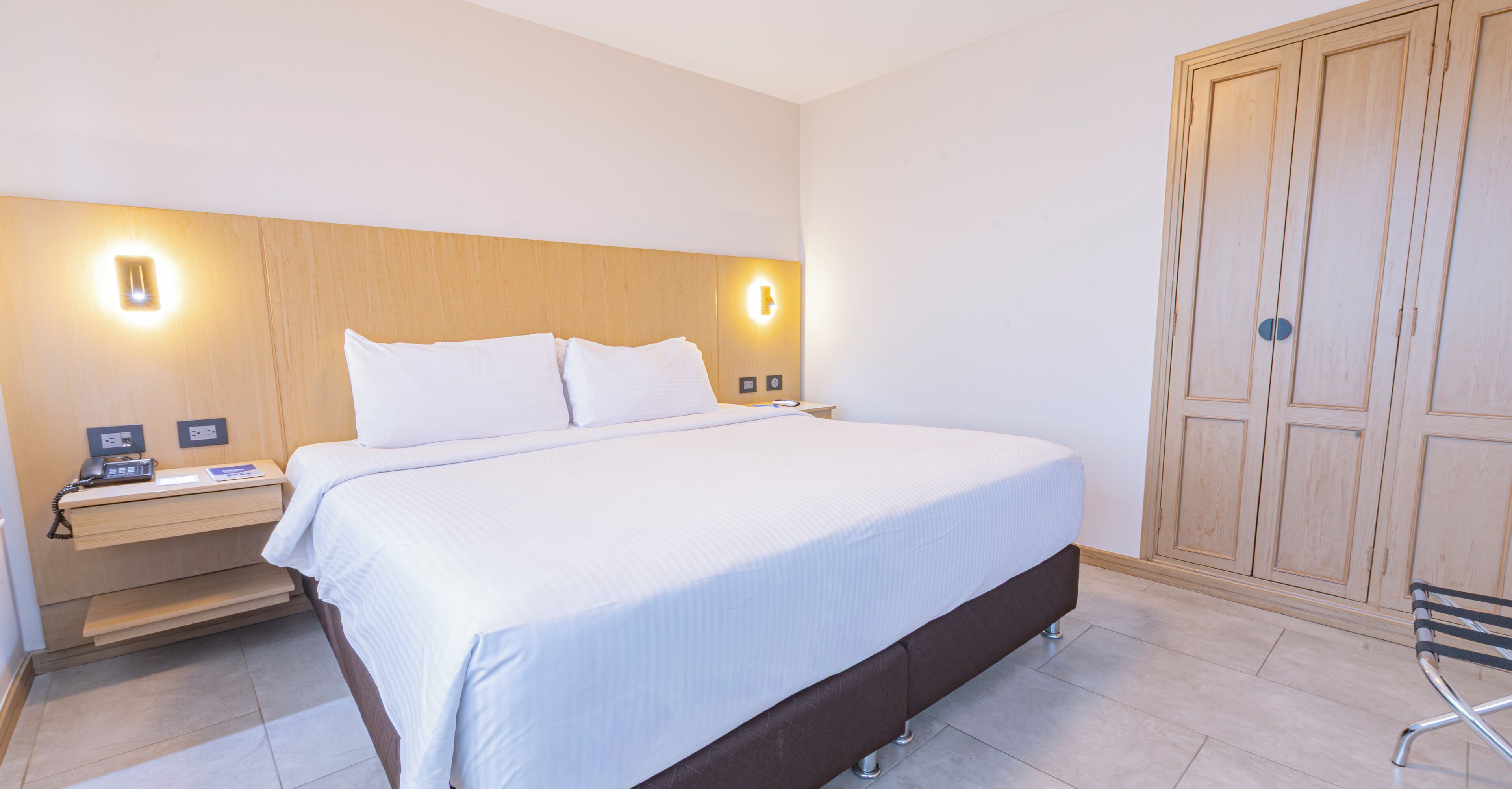 Ein Hotelzimmer mit einem großen Bett, Nachttischen, einem Kleiderschrank und Wandleuchten.