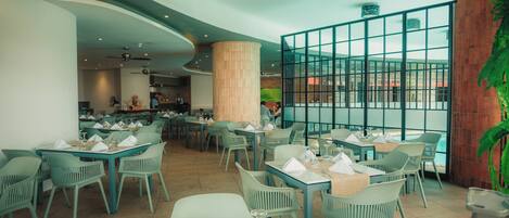 Un restaurant avec des tables et des chaises, une grande colonne et une vue à travers un mur de verre.
