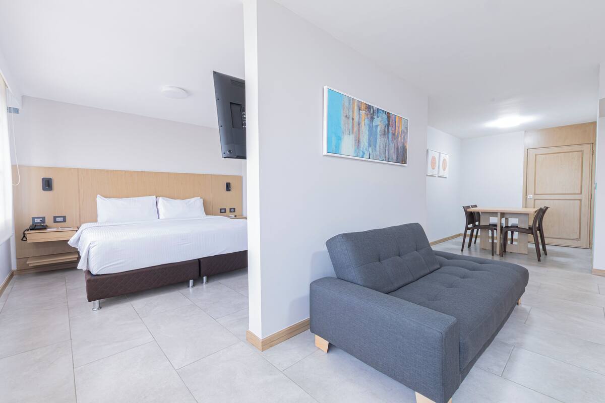 A hotel room with a bed, a sofa, a dining table, and a TV.