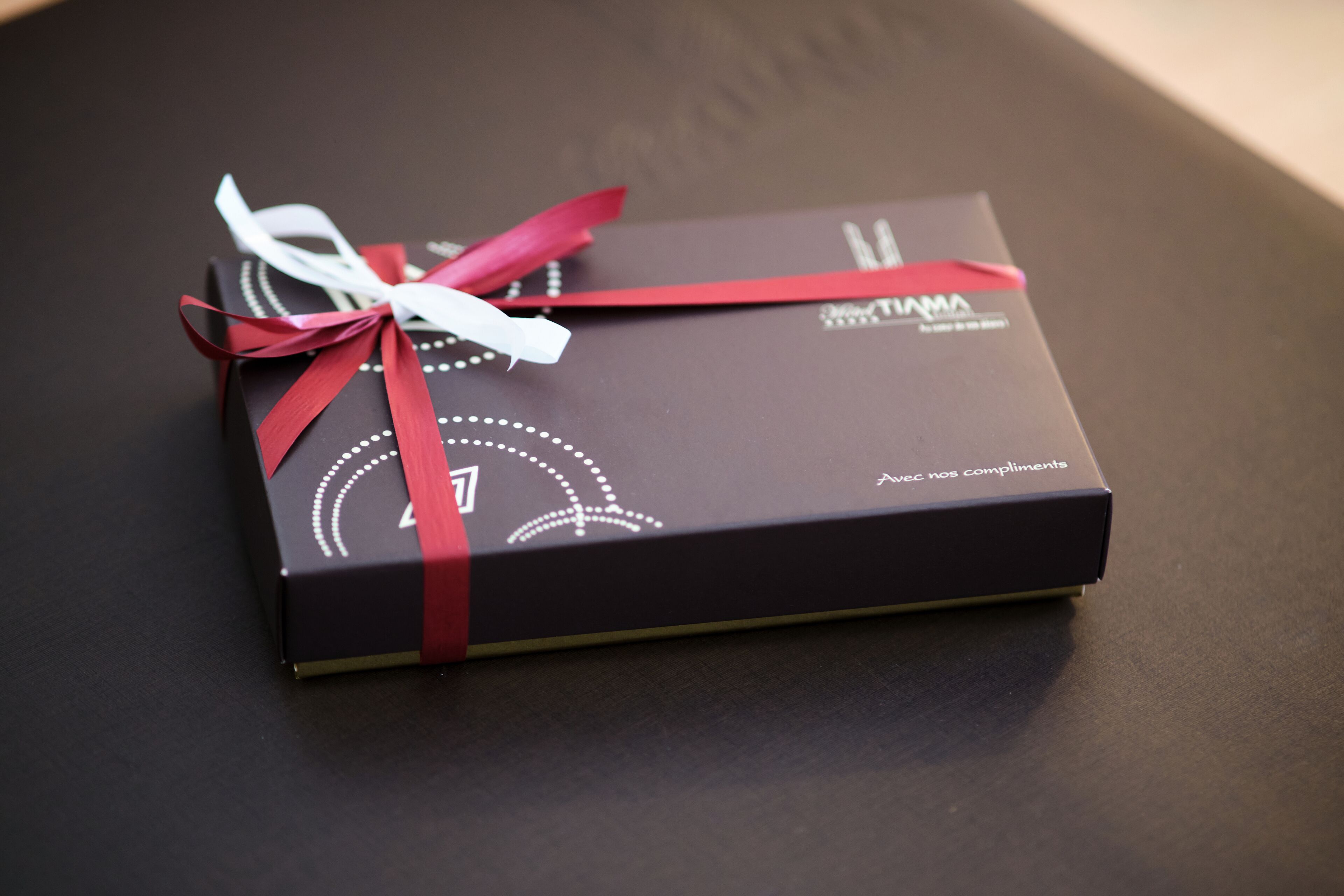Une boîte cadeau noire, ornée d’un ruban rouge, posée sur une surface sombre.