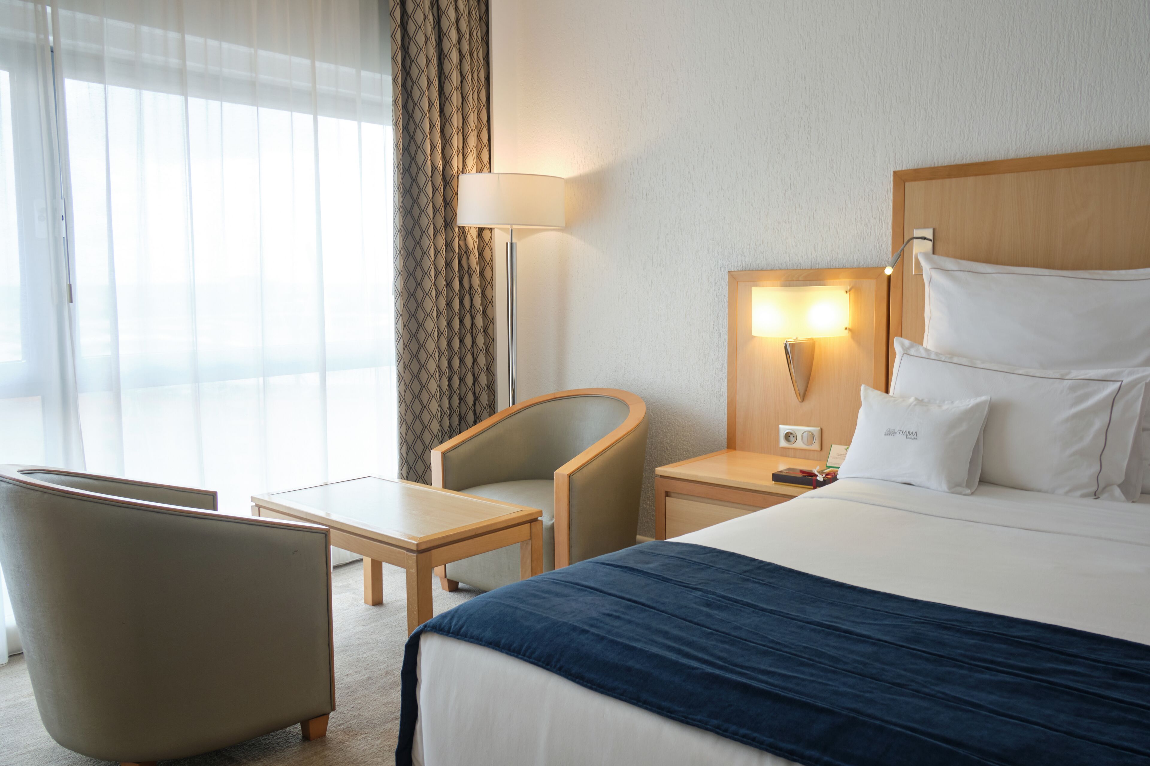 Une chambre d’hôtel équipée d’un lit, d’un bureau, d’une chaise, d’une lampe et offrant une vue sur l’extérieur.