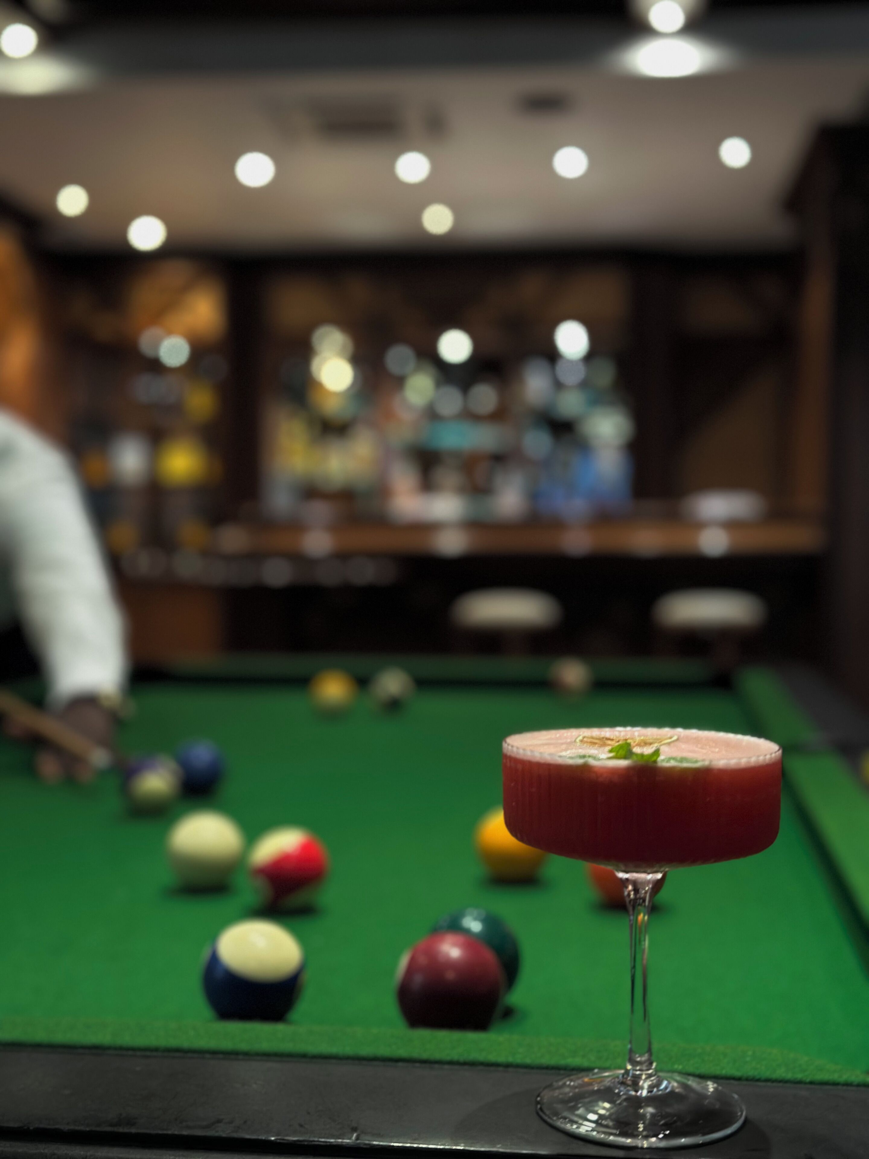 A pool table with a red cocktail in a glass, surrounded by billiard balls.